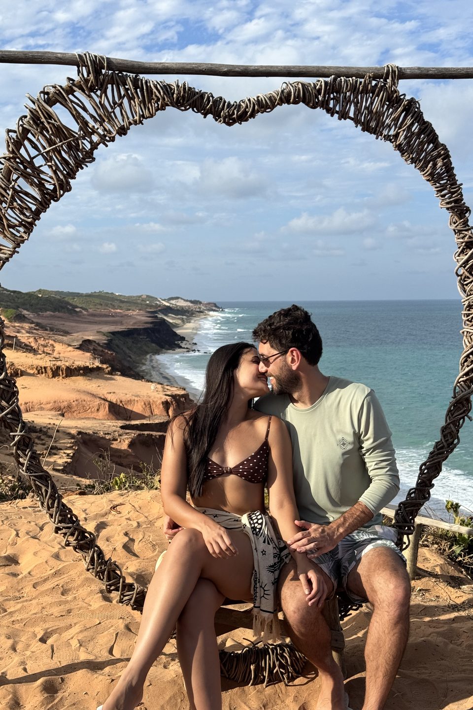 Um beijo emoldurado por um arco de cipó em forma de coração