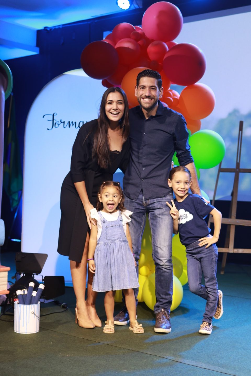 O casal com a Sophia e a Lizzie numa formatura, entre balões