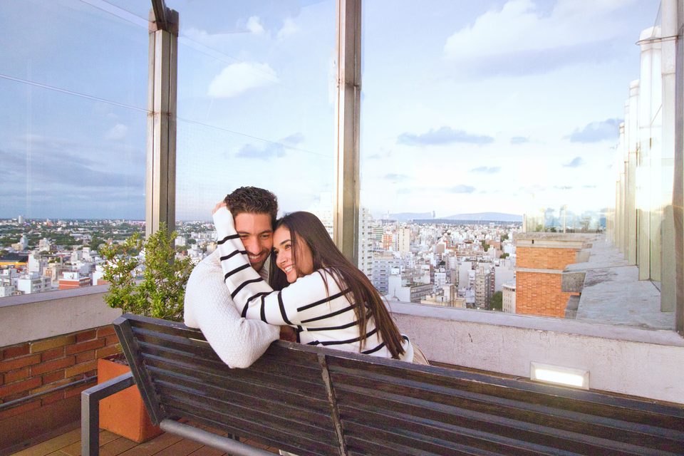O casal abraçado num banco, com a cidade lá embaixo