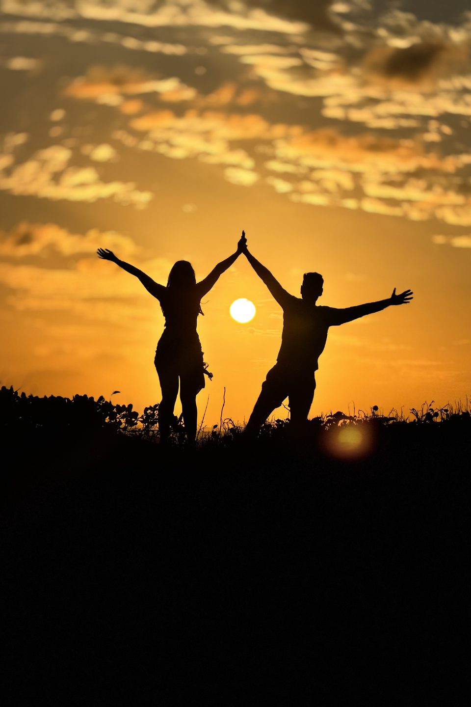 As mãos dadas ao alto, em silhueta, com o sol entre os dois