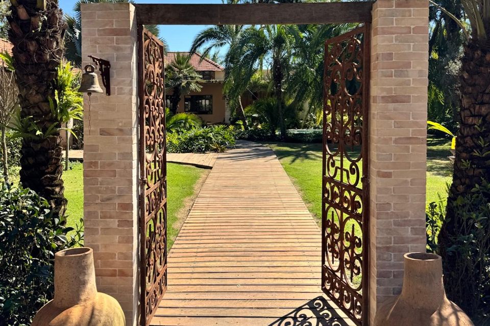 O portão de ferro do Vila La Selva, aberto sobre a passarela de madeira que leva à casa