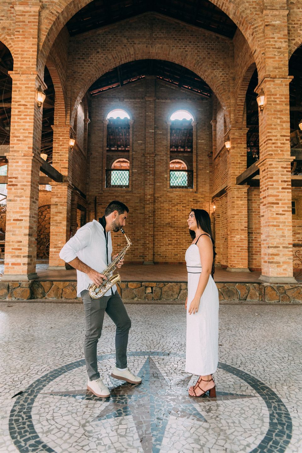 Renan tocando saxofone para Ana embaixo dos arcos de tijolo